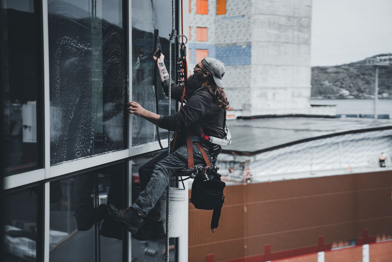 who-we-are A man cleaning skyscraper windows with a harness, showcasing urban high-rise work.